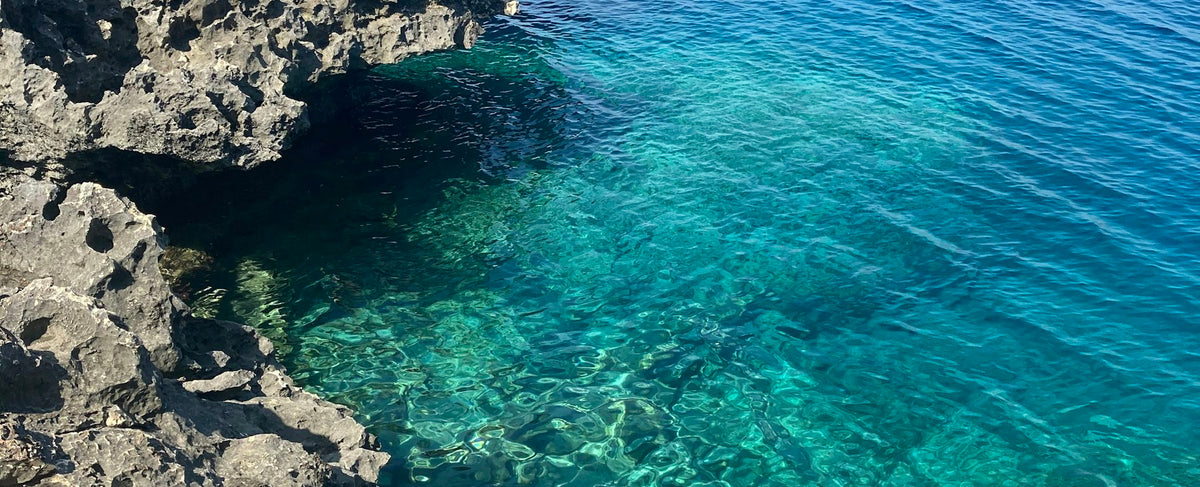 Côte rocheuse méditerranéenne face à une mer bleu profond — l'univers marin d'Acqua di Giò d'Armani selon la parfumerie Olara
