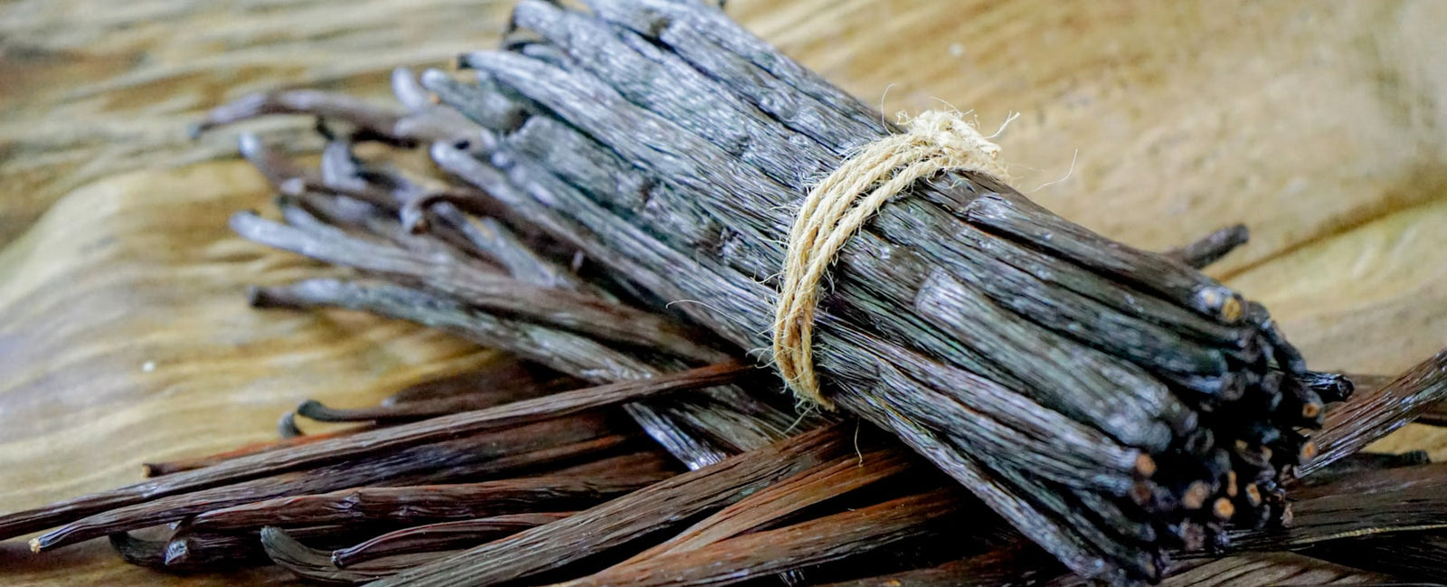 Bouquet de gousses de vanille brunes sur bois — l'or noir de la parfumerie raconté par Olara