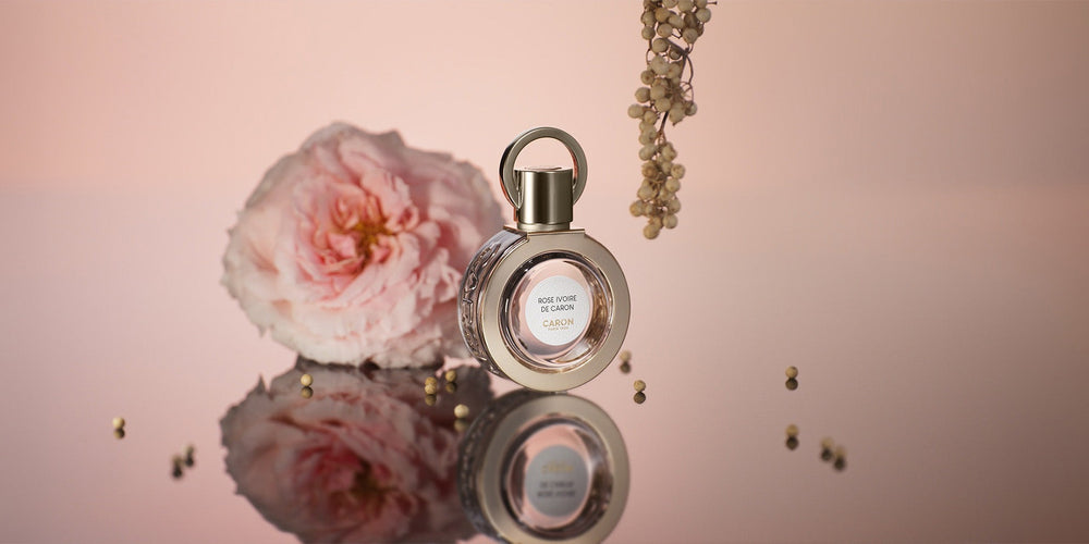 Le flacon de Rose Ivoire de Caron près d’une rose pâle