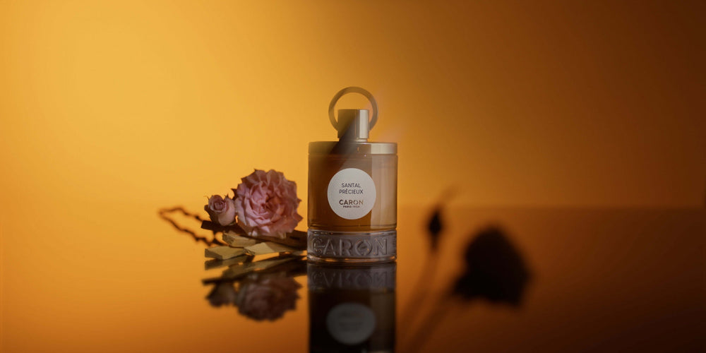 Le flacon de Santal Précieux et une rose sur fond ambré